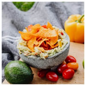 nachos and guacamole in a bowl, along with cherry tomatoes and colored peppers - perfect food for super bowl football party