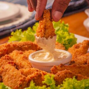 breaded chicken wings being dipped from a bowl of creamy ranch