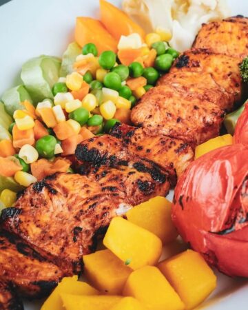 Healthy Homemade Grilled chicken with colorful roasted veggies served in a white ceramic plate.