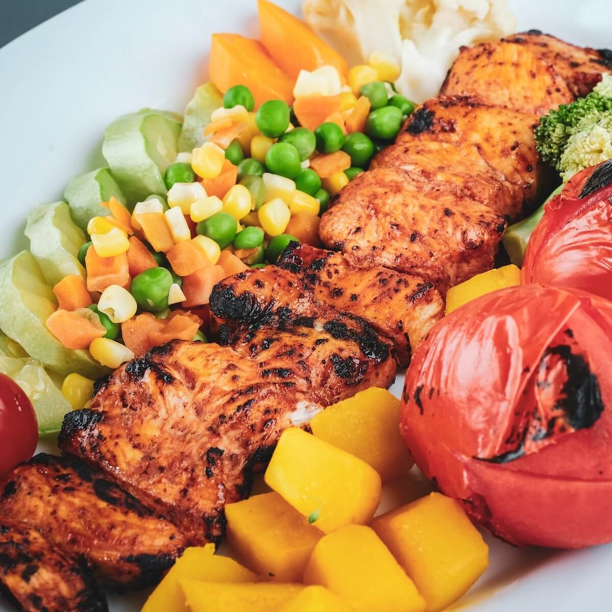 Healthy Homemade Grilled chicken dinner with colorful roasted veggies served in a white ceramic plate.