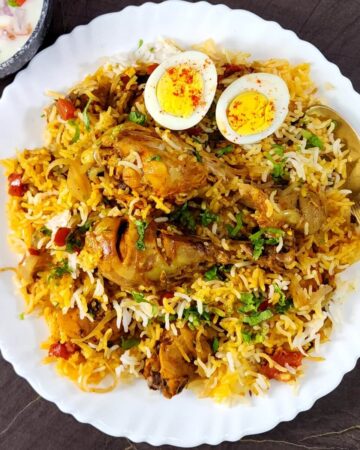 Delicious chicken biryani served in a white plate along with a bowl of raita/yogurt salad.