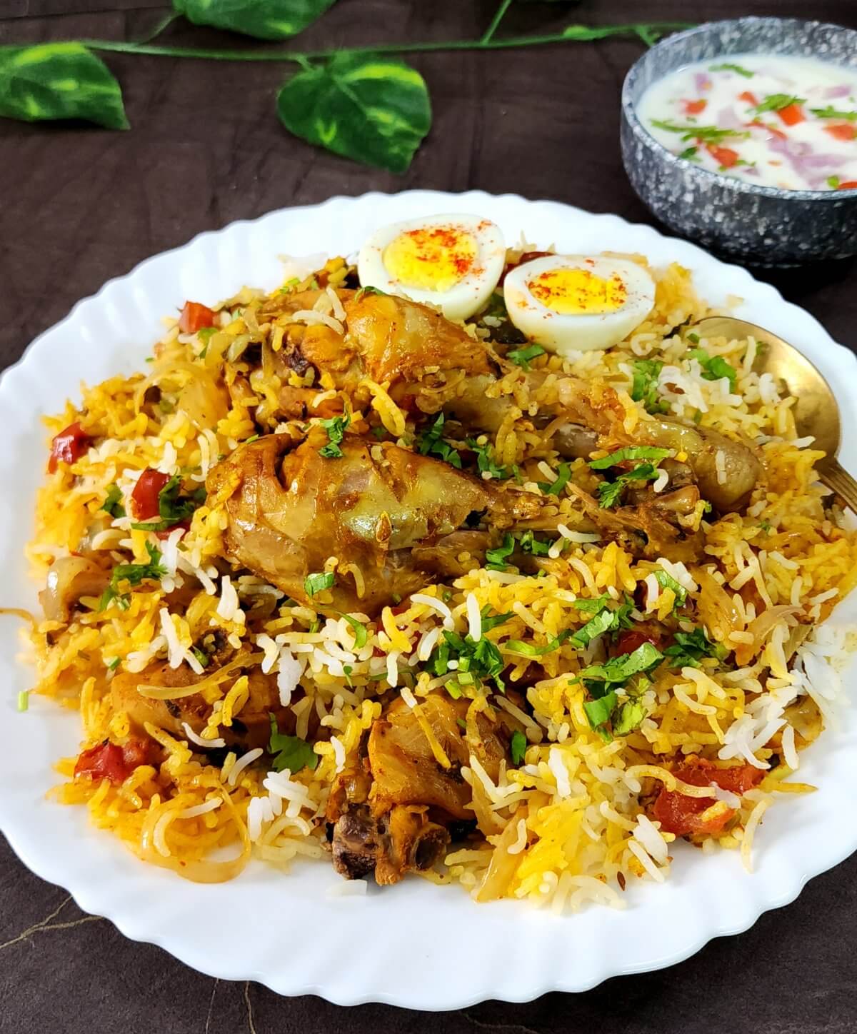 Delicious chicken biryani served on a white ceramic plate with a side of raita.